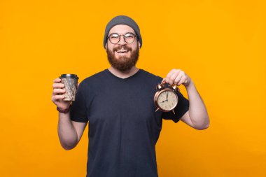 Elinde çalar saat ve kahve fincanı tutan neşeli sakallı hippi portresi. Dinlenme zamanı.