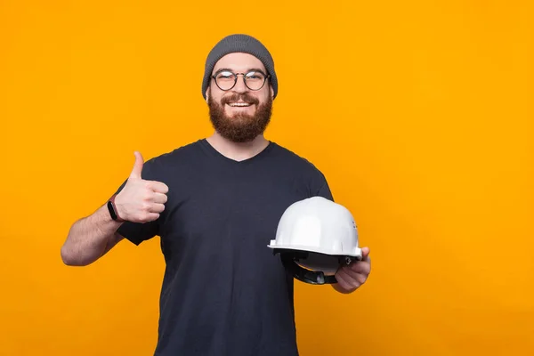 Fénykép vidám szakállas férfi mutatja hüvelykujját fel, és a gazdaság sisak építési — Stock Fotó