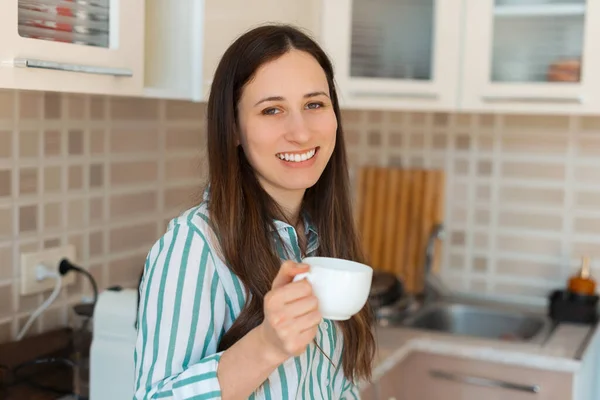 Foto de encantadora jovem mulher em casual segurando xícara de café na cozinha — Fotografia de Stock