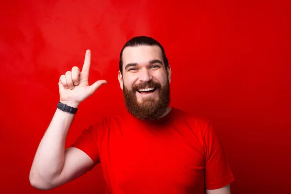 Foto de homem barbudo espantado apontando para cima sobre fundo vermelho — Fotografia de Stock