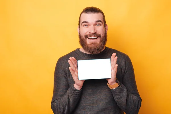 Porträt eines erstaunten gutaussehenden Mannes, der Pullover trägt und den leeren Bildschirm auf dem Tablet vor gelbem Hintergrund zeigt — Stockfoto