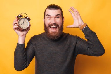 Çalar saat tutan şaşkın sakallı genç adamın portresi.