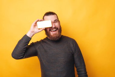 Gözlerinin üzerinde beyaz ekran olan akıllı telefonu tutan hayret dolu gülümseyen genç adamın portresi
