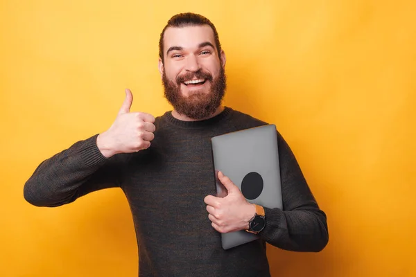 Photo de jeune homme joyeux avec la barbe montrant pouce vers le haut et tenant ordinateur portable — Photo