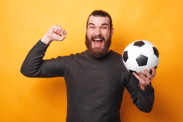 Zdjęcie zdumionego człowieka wspierającego jego ulubioną drużynę i trzymającego piłkę nożną — Zdjęcie stockowe