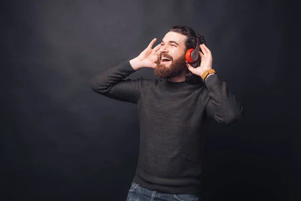 Foto de hombre guapo feliz escuchando música en los auriculares sobre fondo negro —  Fotos de Stock