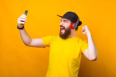 Akıllı telefon kullanan ve kulaklıkta müzik dinleyen sakallı bir adamın portresi.