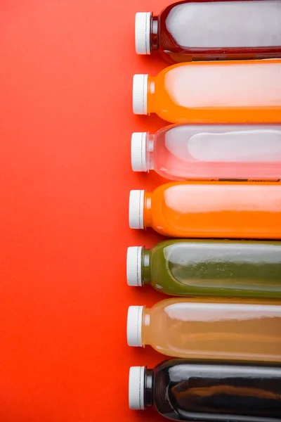 Foto de muchas botellas de jugo fresco de desintoxicación en fila sobre fondo rojo — Foto de Stock