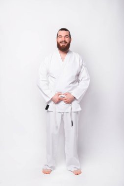 Beyaz arka planda duran tekvando üniformalı sporcunun tam boy fotoğrafı.