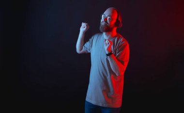Yakışıklı genç sakallı hippi adamın fotoğrafı müzik dinliyor ve kırmızı ve mavi ışıklarla arka planda dans ediyor.