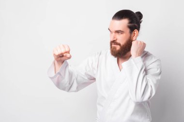 Beyaz arka planda tekvando üniforması giyen sakallı bir adamın fotoğrafı.