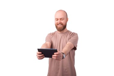 Sakallı mutlu genç adam tablette online oyunlar oynuyor.