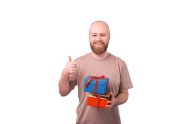 Sakallı, neşeli, gülümseyen genç bir adam hediye kutusu tutuyor ve başparmağını kaldırıyor, hoşuma gidiyor.