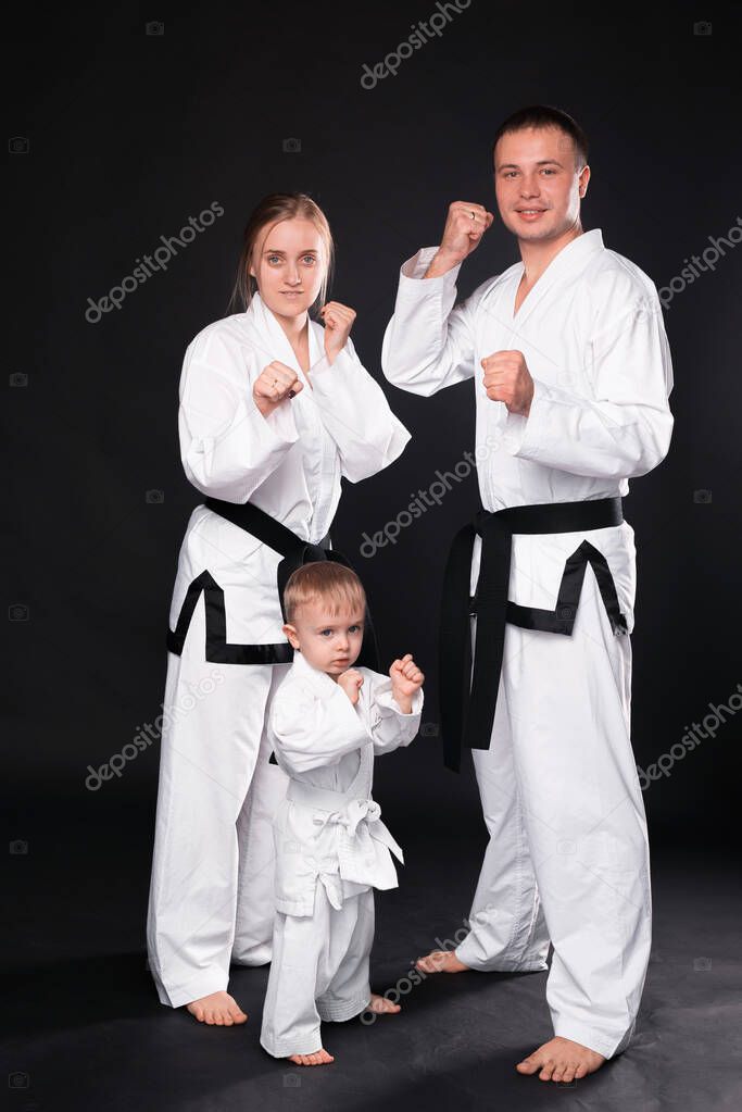 Portrait of happy young family in martial arts uniform standing over black background