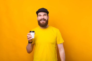 Joyful young bearded hipster man drinking cup of coffee on the go.