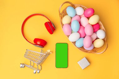 Top view of easter eggs smartphone with green screen and shopping basket.
