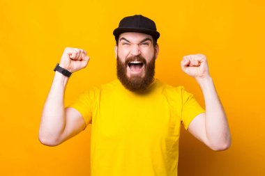 Şaşırmış sakallı adam bağırıyor ve sarı arka plandaki zaferi kutluyor..