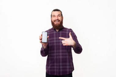 Akıllı telefonu işaret eden sakallı hayret verici genç adam..