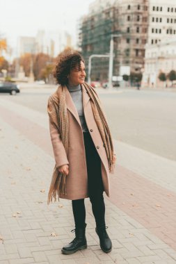 Şehir sokaklarında yürüyen ve gülümseyen, paltolu neşeli, neşeli genç bir kadının fotoğrafı..