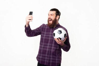 Akıllı telefon kullanan ve futbol topu tutan sakallı adamın fotoğrafı. Gol, takımını destekle..