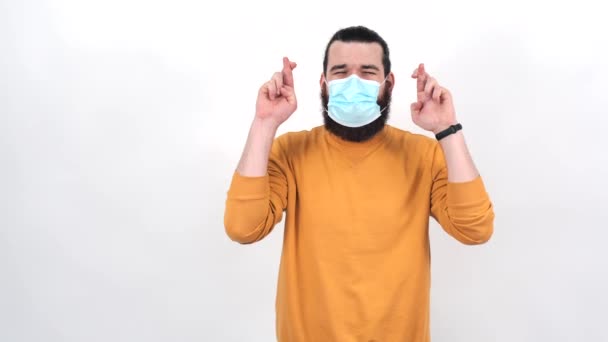 Filmación de un joven cruzando dedos y usando mascarilla facial medicinal — Vídeos de Stock