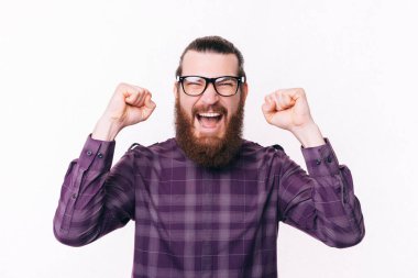 Gözlük takan ve kollarını kaldırıp kutlama yapan sakallı bir adamın fotoğrafı..