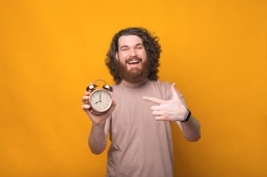 Sarı arka planda alarma bakan uzun saçlı heyecanlı genç sakallı adamın fotoğrafı..