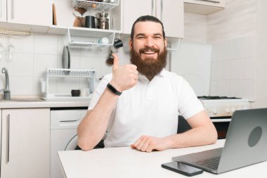 Evinde dizüstü bilgisayarla çalışan neşeli, sakallı genç bir adam..