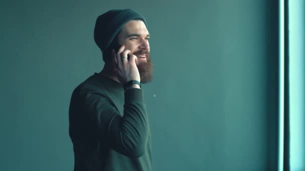 Πλάνα από χαρούμενα hipster γενειοφόρος άνθρωπος μιλάμε σε smartphone εσωτερική — Αρχείο Βίντεο