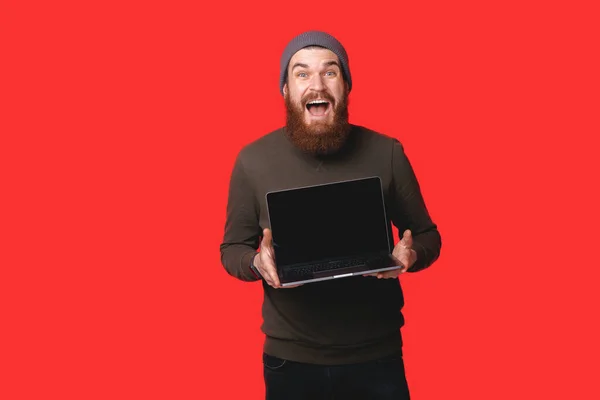 Lenyűgöző Szakállas Hipster Férfi Mutatja Laptop Felett Piros Háttér — Stock Fotó