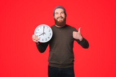 Büyük beyaz bir saat tutan ve kameraya gülümseyen bir adamın güzel bir fotoğrafı. .