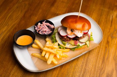 Beyaz tabakta karidesli bir hamburgerin resminin tamamında patates kızartması da var. Hepsi ahşap bir masada..