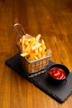 Patates kızartması ve ahşap bir masada ketçap kaplı bir sepetin dikey fotoğrafı..