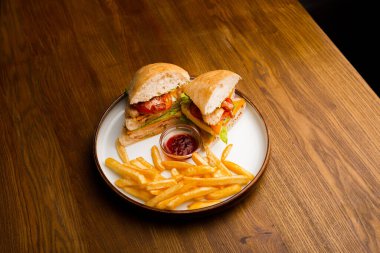 Tahta bir masanın üstünde sandviç ve patates kızartması tabağı.