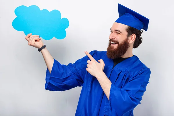 Šťastný Vousatý Muž Modrém Maturitním Hábitu Drží Bublinu Mraků Ukazuje — Stock fotografie