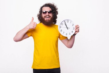 Mutlu sakallı bir adam büyük beyaz bir saat tutuyor ve gülümsüyor. .