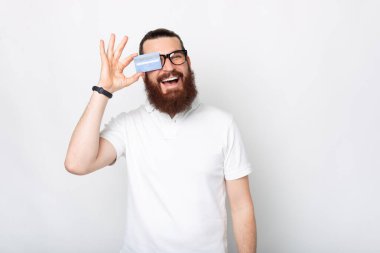 Kameraya gülümseyen bir adamın fotoğrafı. Gözlerinin yanında kredi kartı tutuyor. .