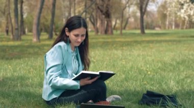 Sıradan bir kadının parkta çimlere oturup kitap okuduğu bir görüntü.
