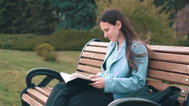 Bilder på en ung kvinna som sitter på bänk i parkens läsbok — Stockvideo