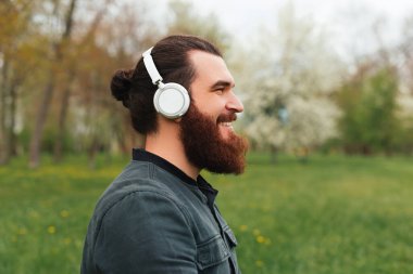 Beyaz kablosuz kulaklıklarda müzik dinleyen sakallı hippi portresi..