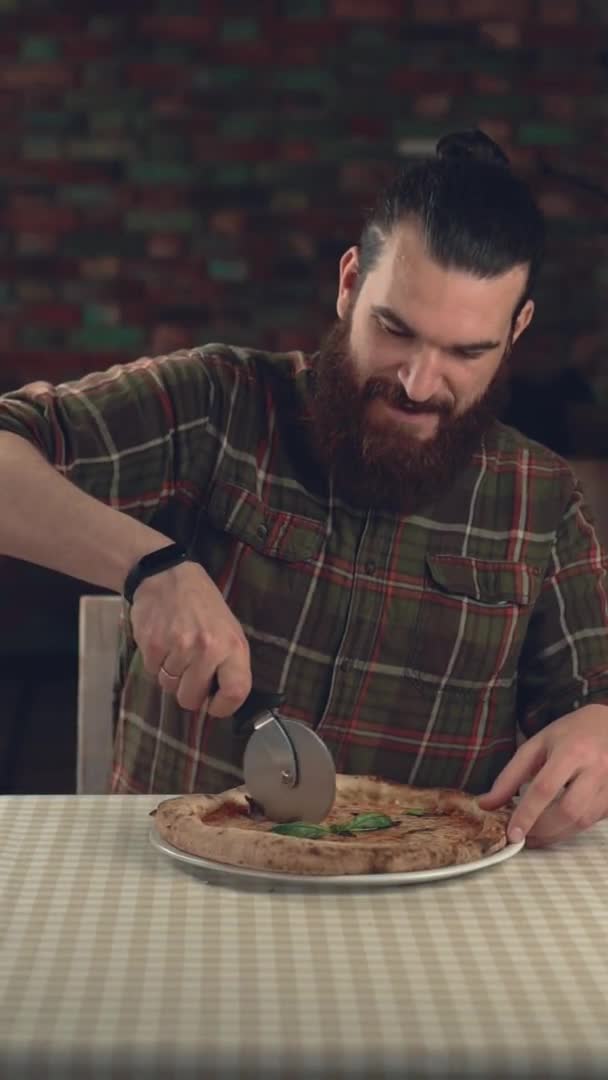 Imágenes verticales en cámara lenta del hombre barbudo cortando pizza en el restaurante — Vídeos de Stock