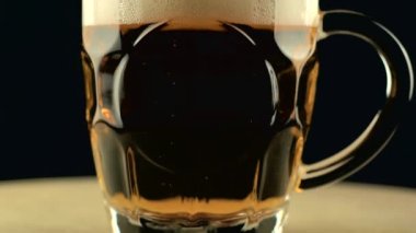 Koyu arka planda köpüklü dolu bira bardağının görüntüsü.