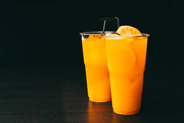 Photo of two orange lemonades on dark table over black background.