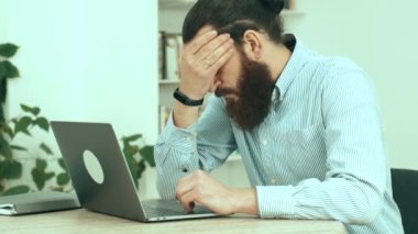 Dizüstü bilgisayarın önünde oturan yorgun ofis çalışanının görüntüsü.