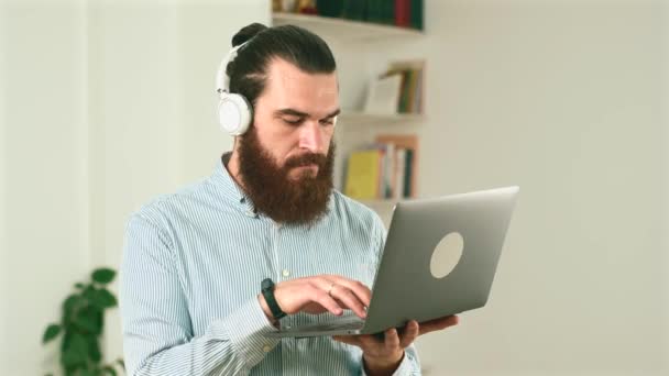 Footage of bearded man standing in office and typing on laptop — Stock Video