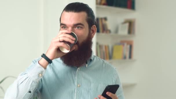 Κοντινό πλάνο του γενειοφόρου άντρα στο γραφείο πίνοντας καφέ και χρησιμοποιώντας smartphone — Αρχείο Βίντεο