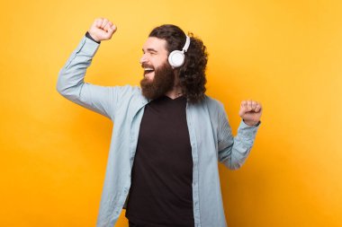 Beyaz kablosuz kulaklıklarda müzik dinleyen neşeli, yakışıklı sakallı hippi..