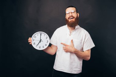 Büyük beyaz saati işaret eden sakallı hippi adamın fotoğrafı..