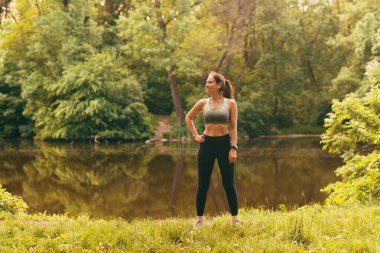 Gün batımında gölün kenarında duran zayıf, formda, genç bir kadının fotoğrafı..