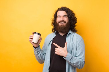 Sarı arka planda kağıt kahve bardağını gösteren uzun saçlı genç sakallı hippi..